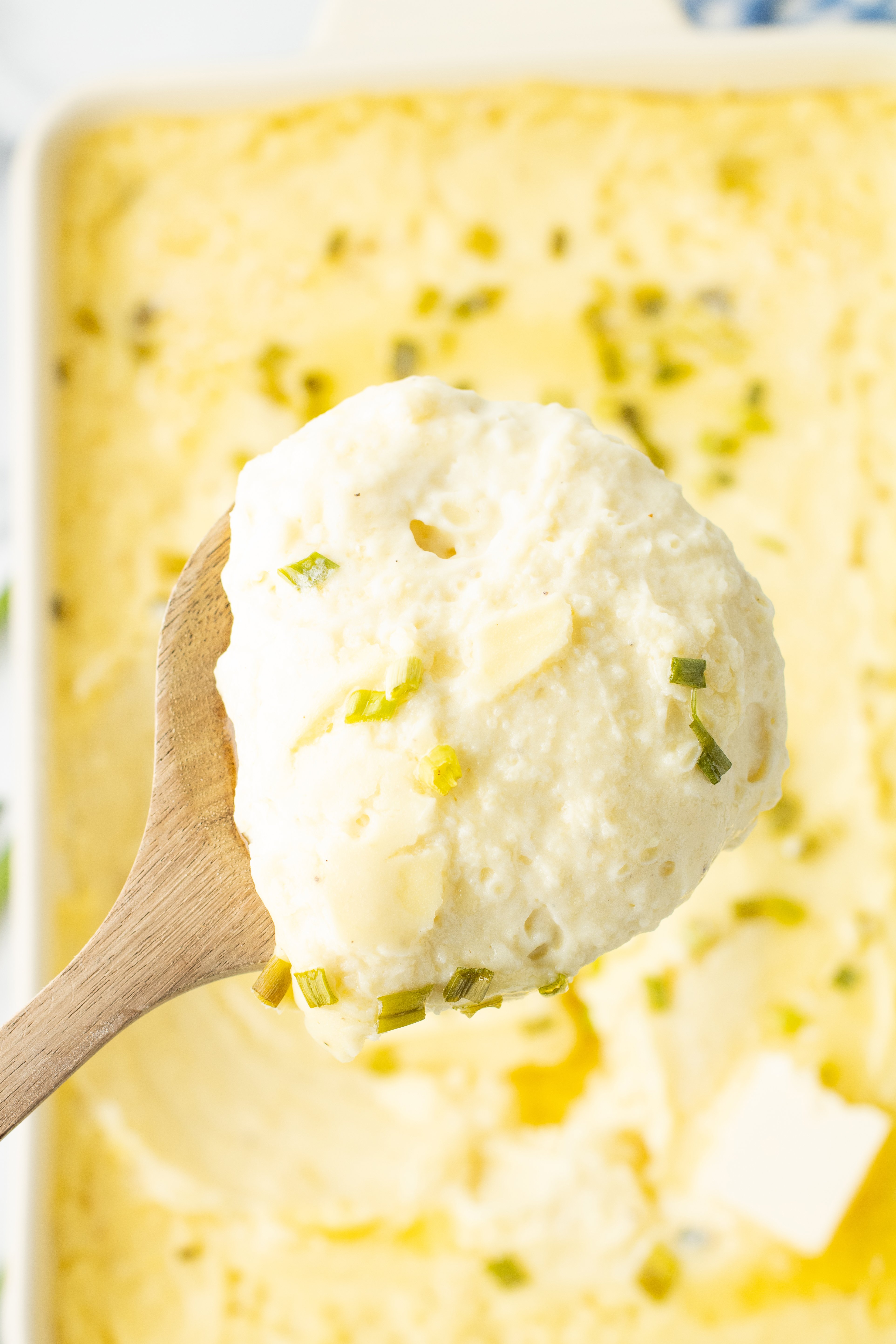 a wooden spoon full of cream cheese mashed potatoes over the baking dish