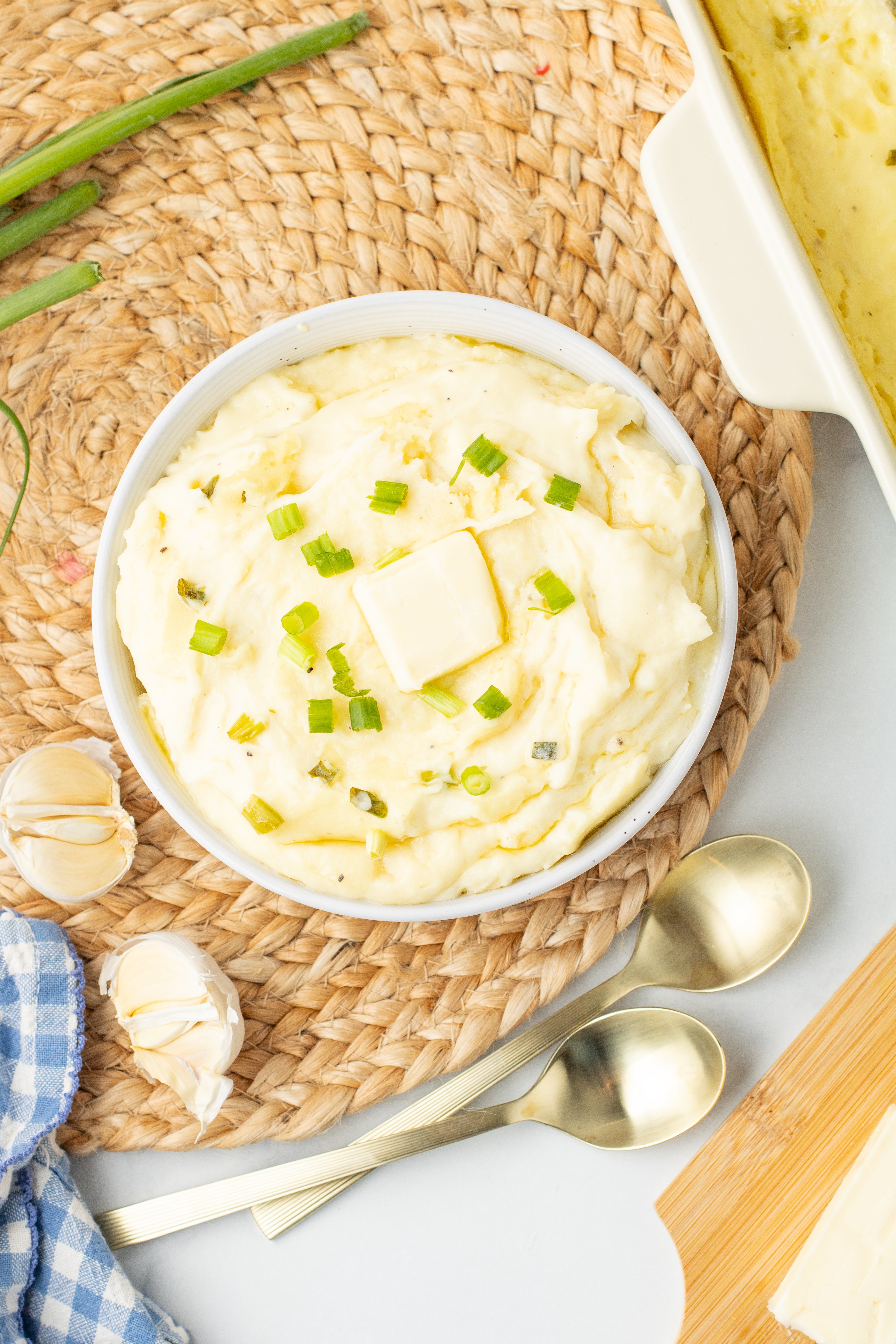 mashed potatoes with cream cheese in a white bowl topped with butter and chives