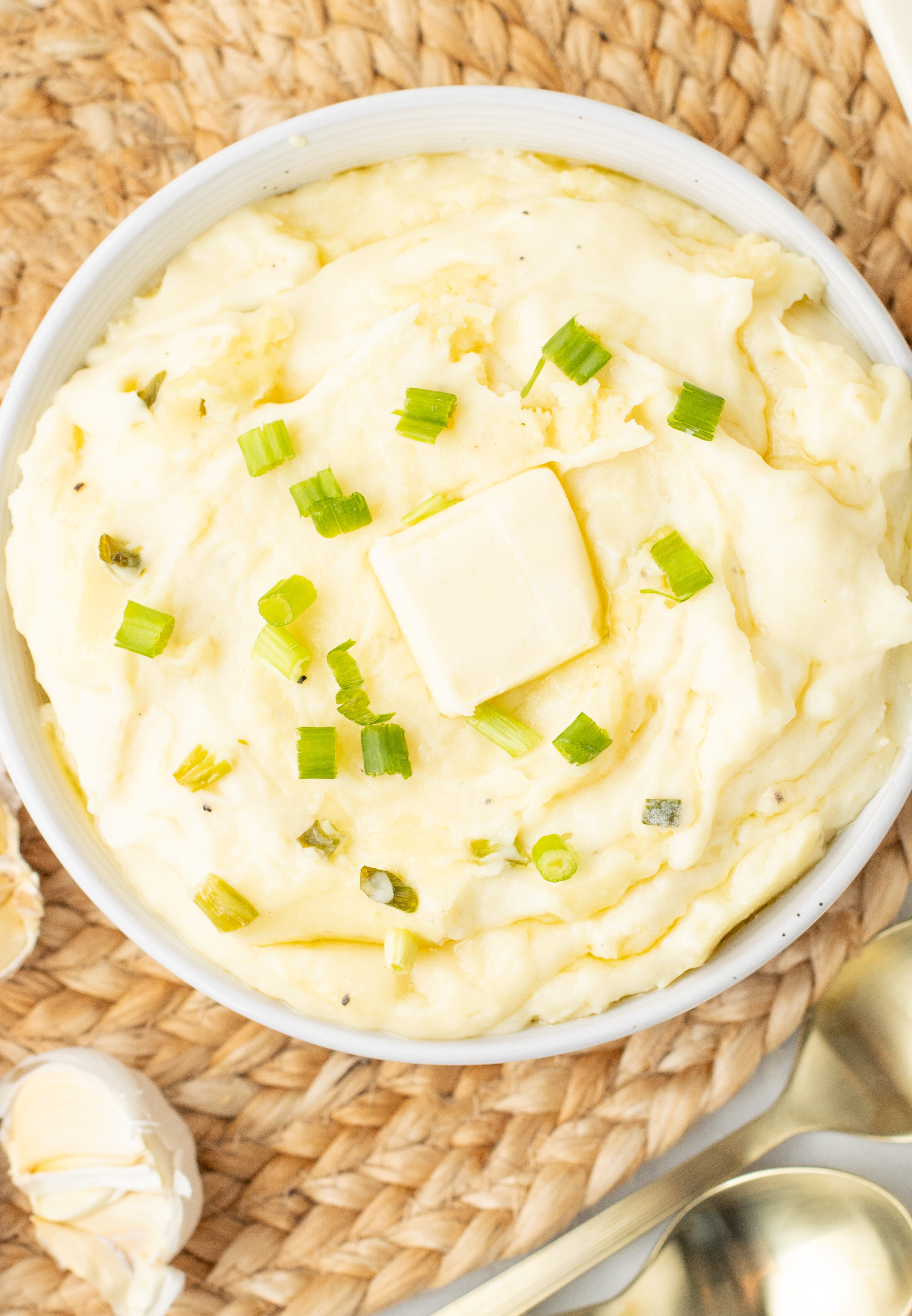 mashed potatoes with cream cheese in a white bowl topped with butter and chives