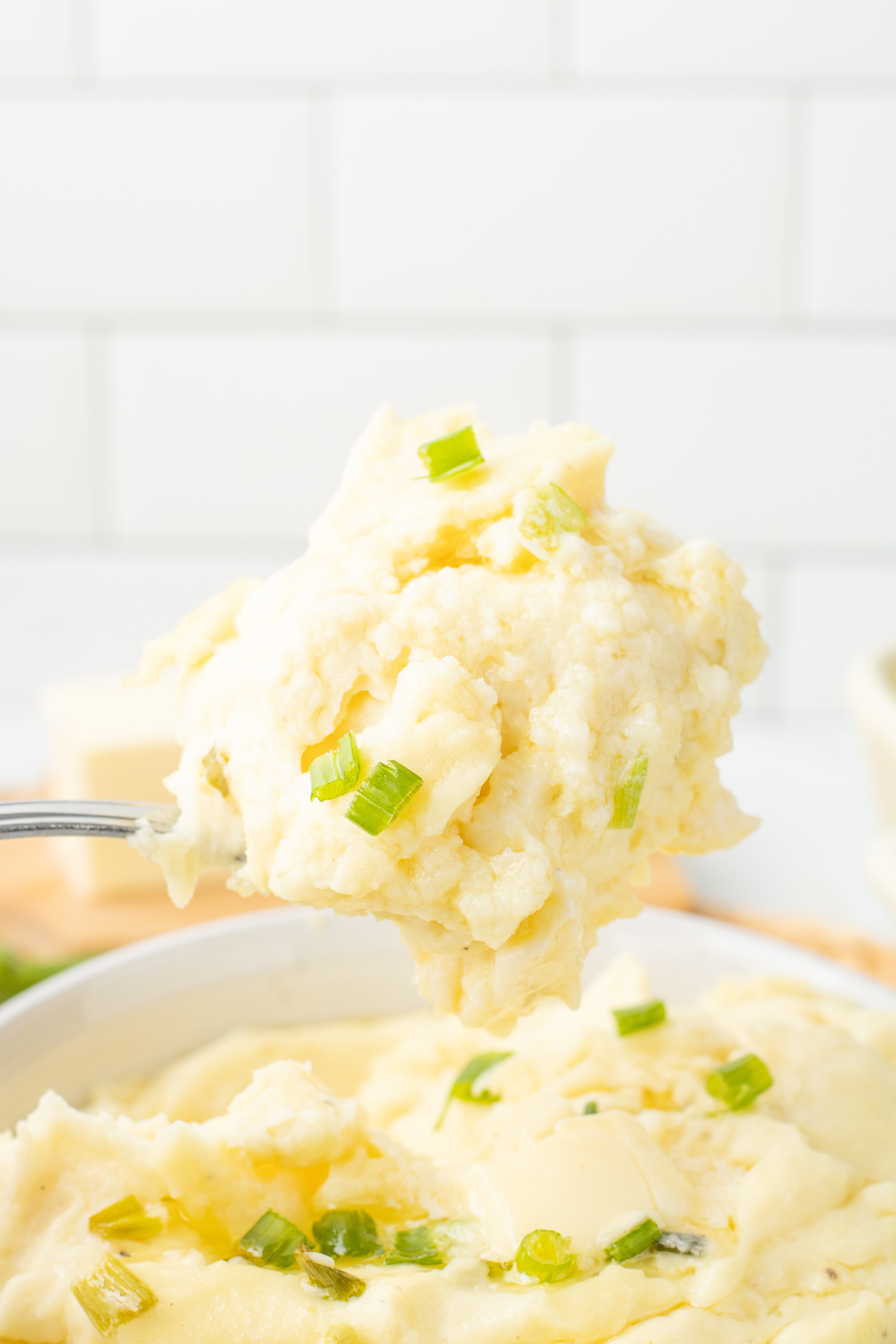 a spoon full of cream cheese mashed potatoes over the baking dish