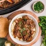 slow cooker steak bites over mashed potatoes in a white bowl