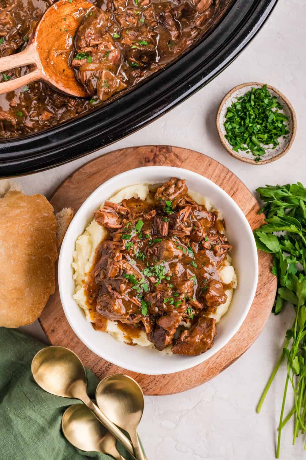cooked garlic butter steak bites over mashed potatoes in a bowl next to more steak bites in slow cooker