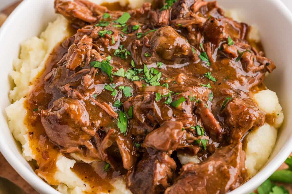 bowl of slow cooker steak bites over mashed potatoes in a white bowl