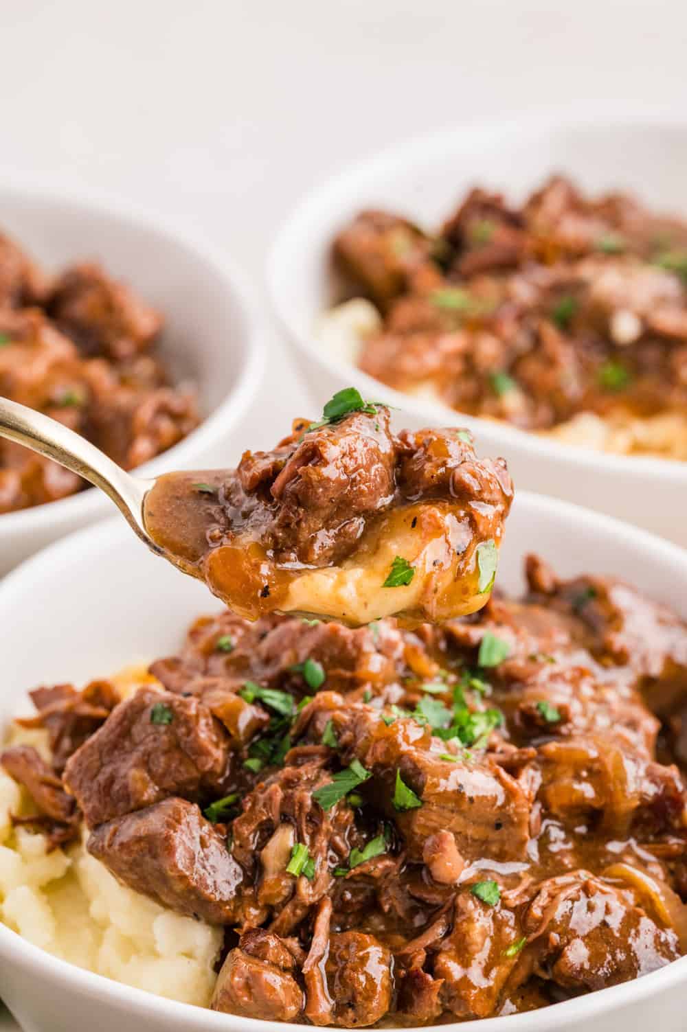 crockpot steak bites over mashed potatoes with a spoonful above the bowl