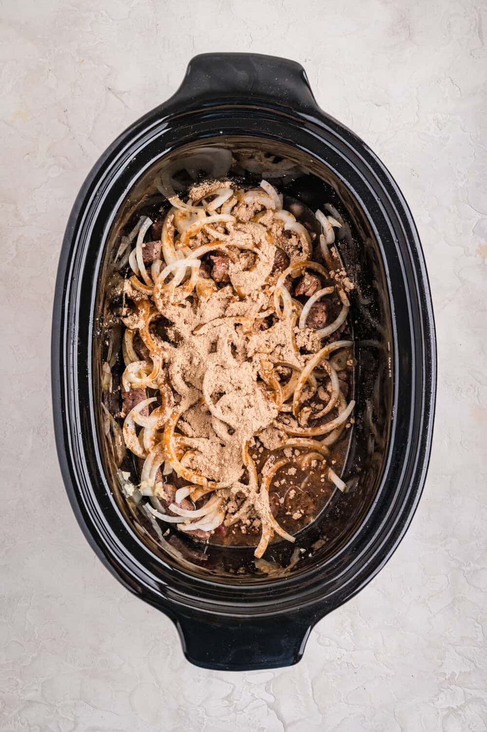 onions added to beef cubes in slow cooker