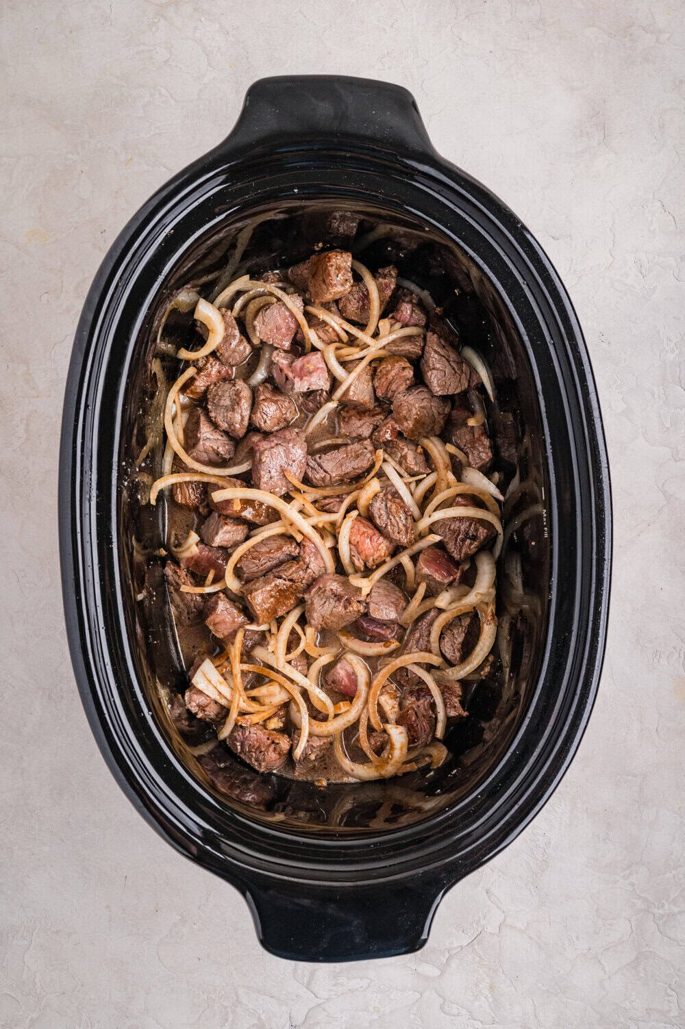 cooked steak bites in slow cooker pot with onions and seasonings