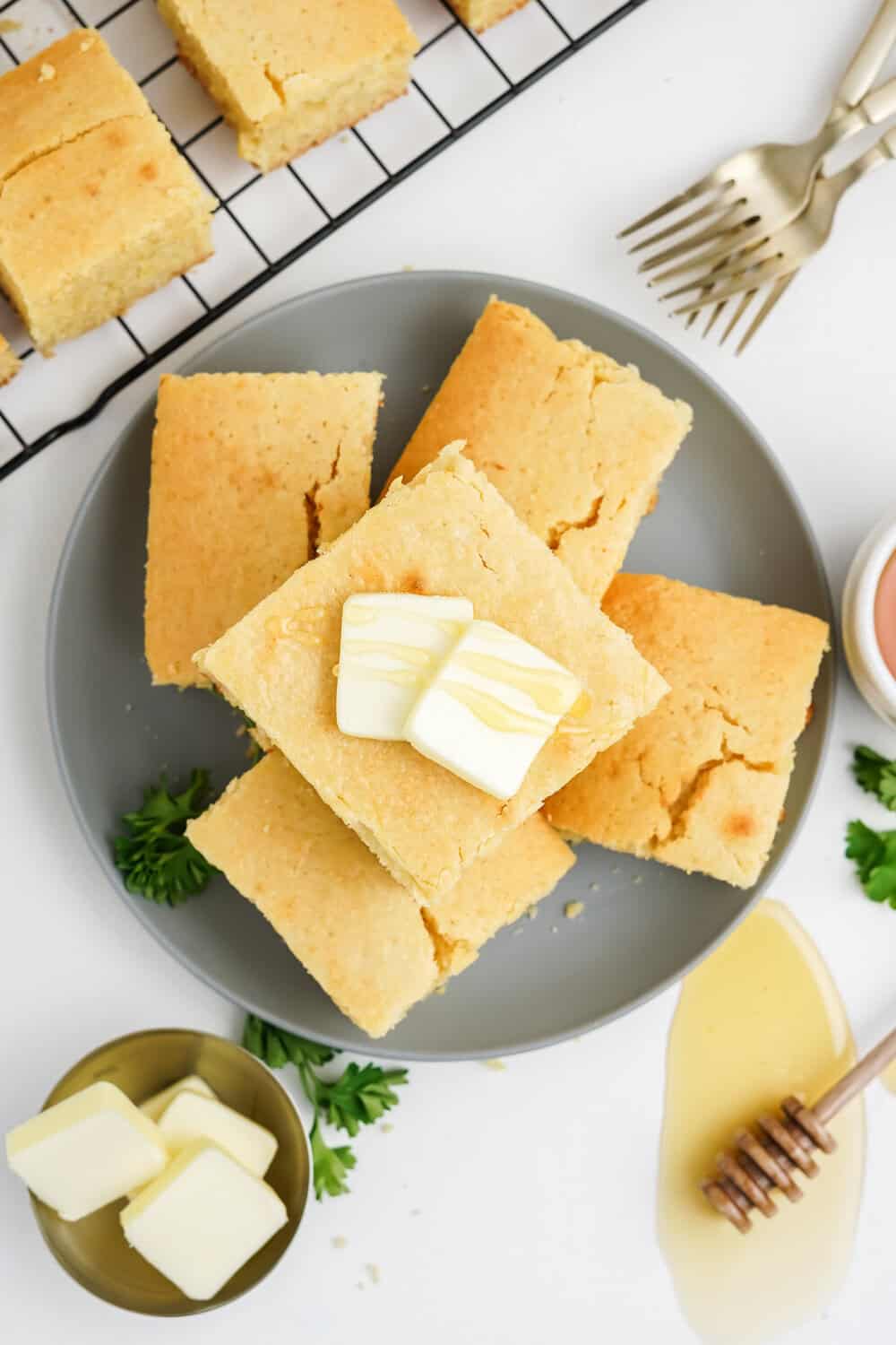 squares of honey cornbread stacked on a plate with butter and honey