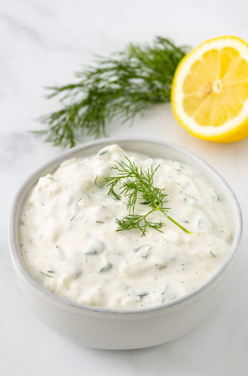 Tzatziki sauce in a white bowl with fresh dill and a lemon