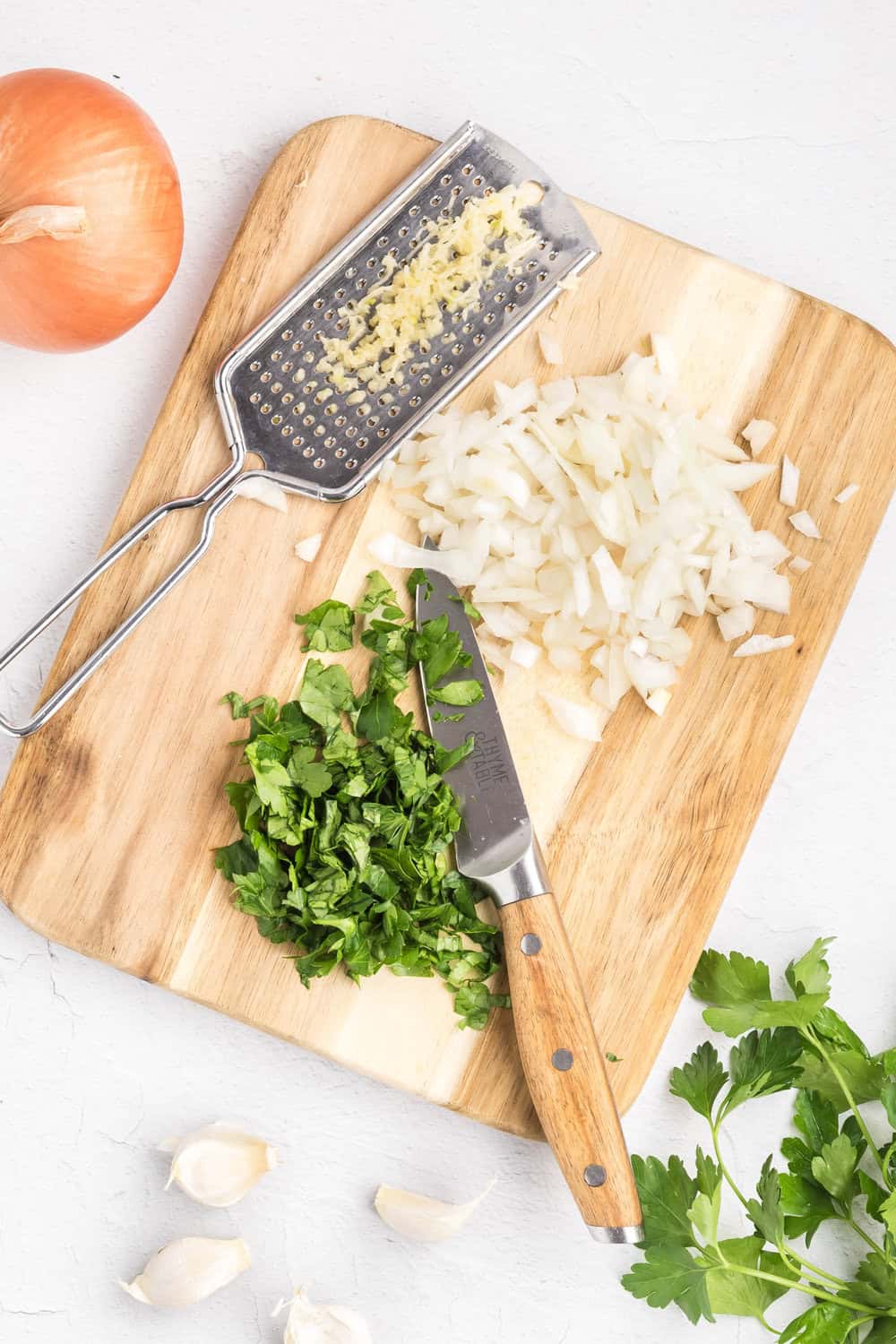 chopped parsley and onion, minced garlic - all on a cutting board with a knife