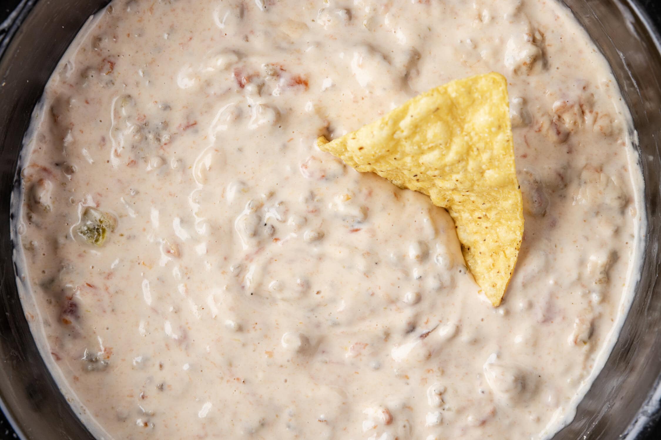 rotel sausage dip in slow cooker with a chip being dipped