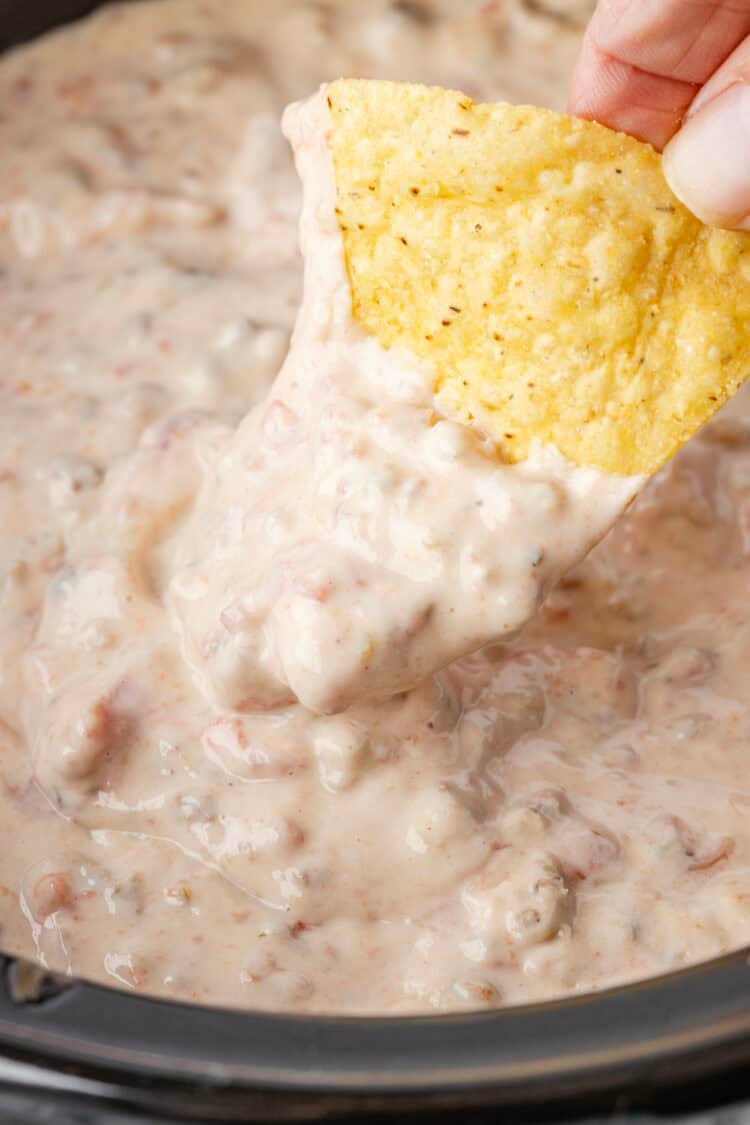 rotel sausage dip in slow cooker with a chip being dipped