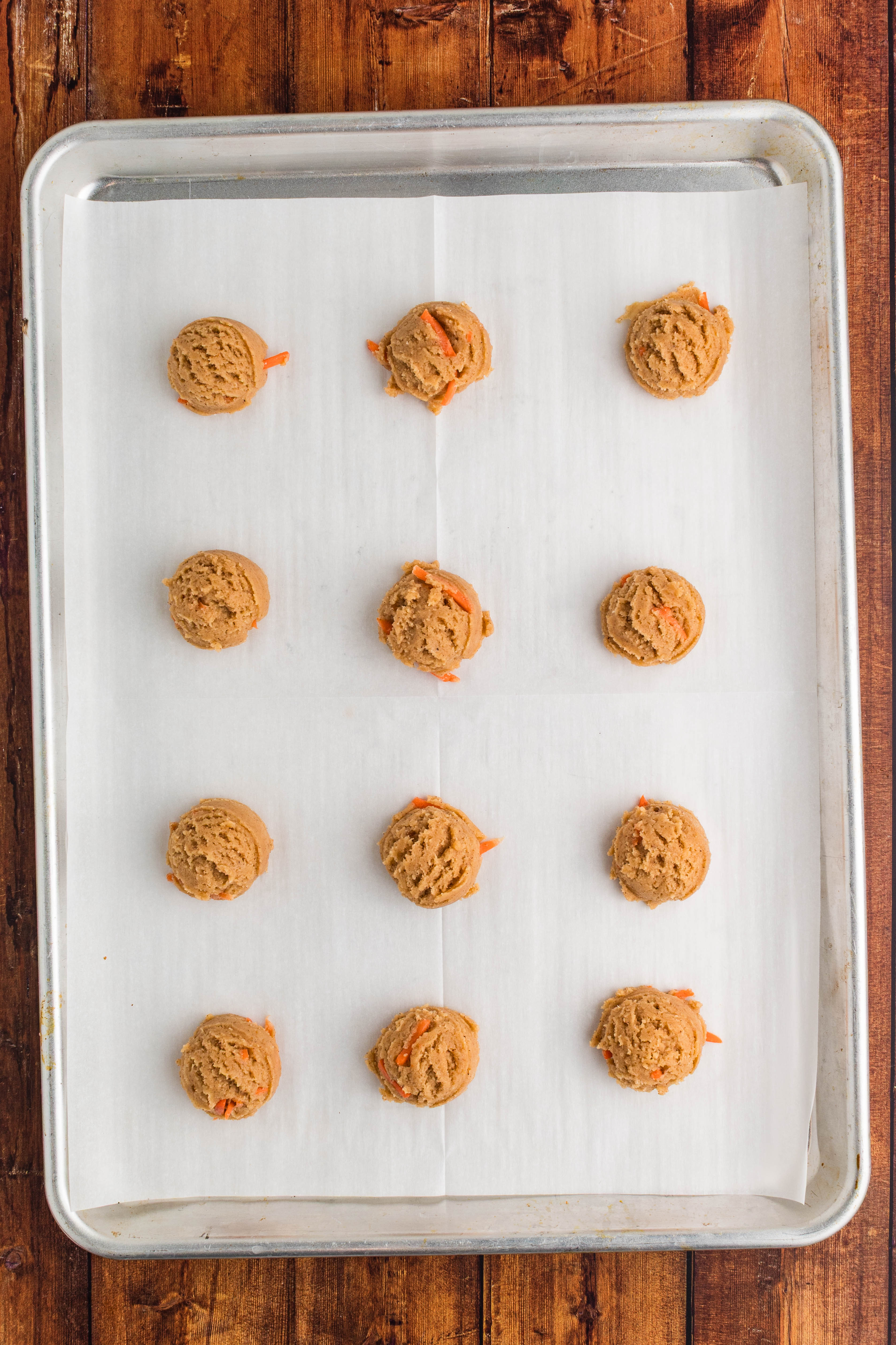carrot cake cookie dough scooped onto lined baking sheet