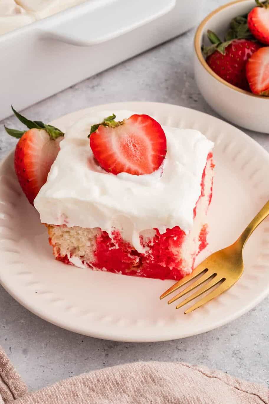 slice of strawberry poke cake on a white plate with a fork