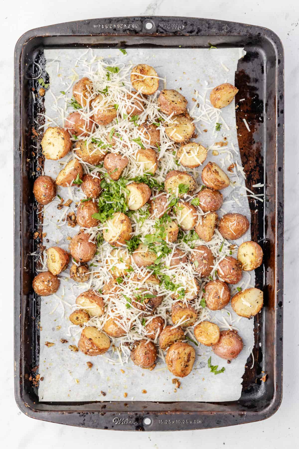 roasted garlic parmesan potatoes on a baking sheet topped with extra parmesan and parsley