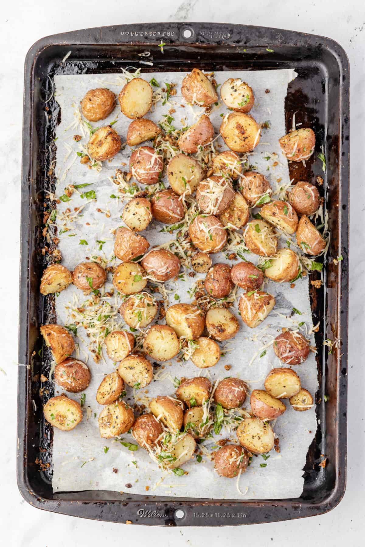 roasted garlic parmesan potatoes on a baking sheet tossed with extra parmesan and parsley