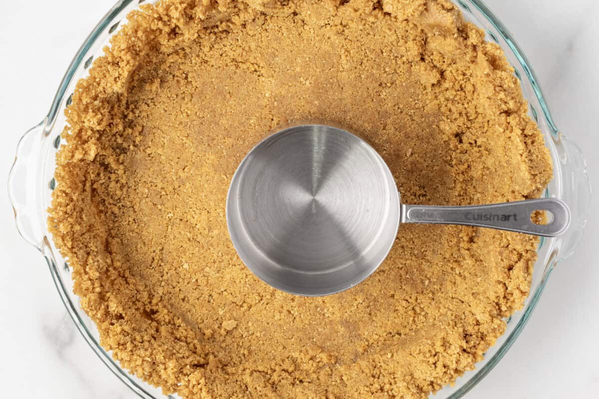 graham crackeer pie crust with a measuring cup in the middle