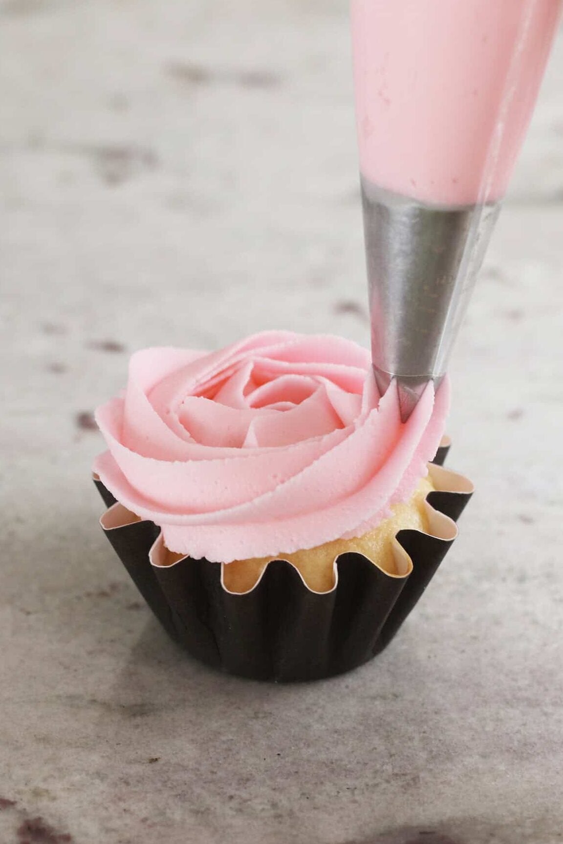 piping cream cheese frosting on a cupcake