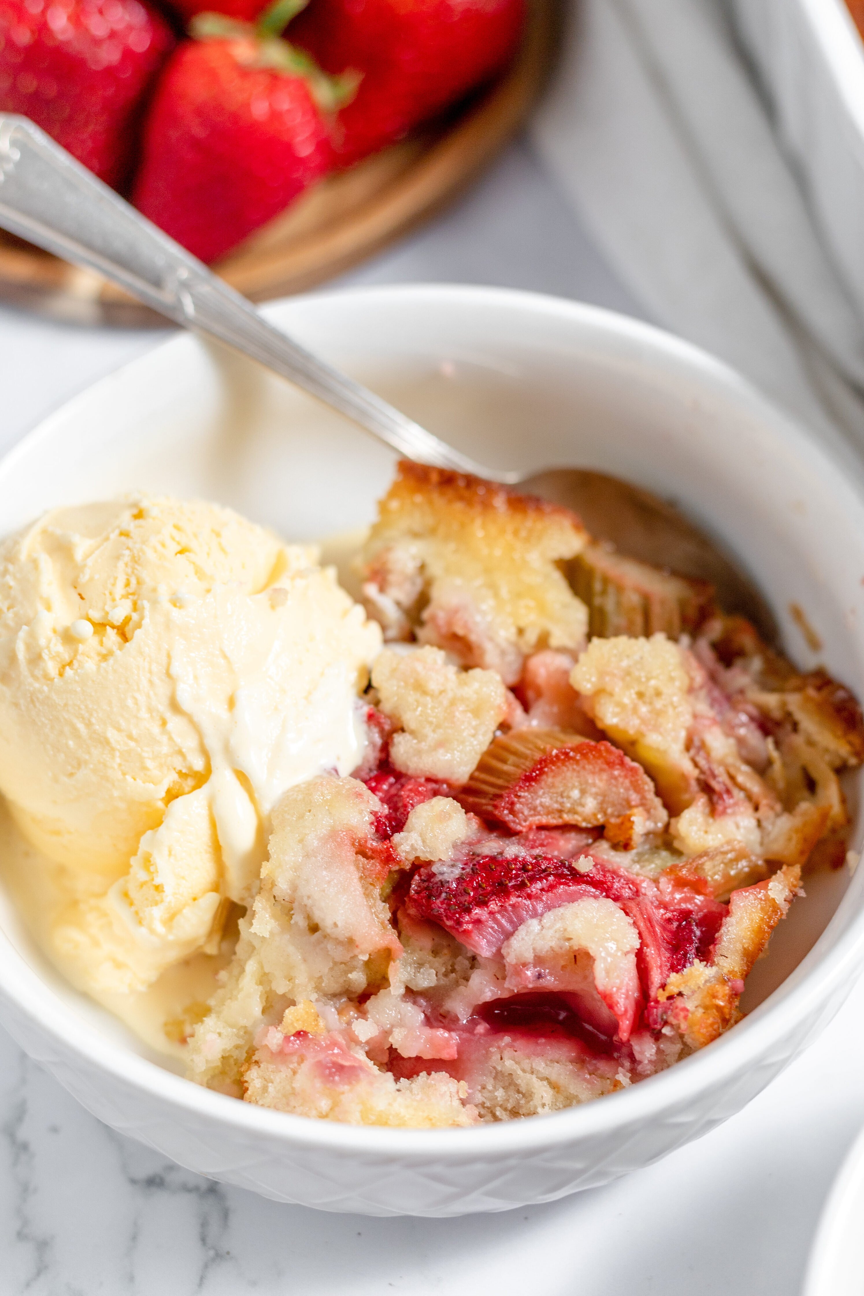 strawberry rhubarb cobbler in a bowl with vanilla ice cream