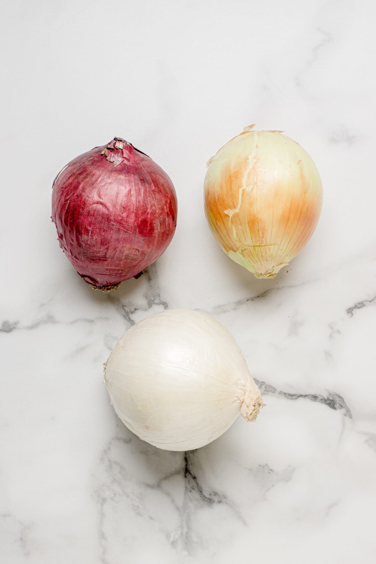 red onion, yellow onion, and white onion on a white surface