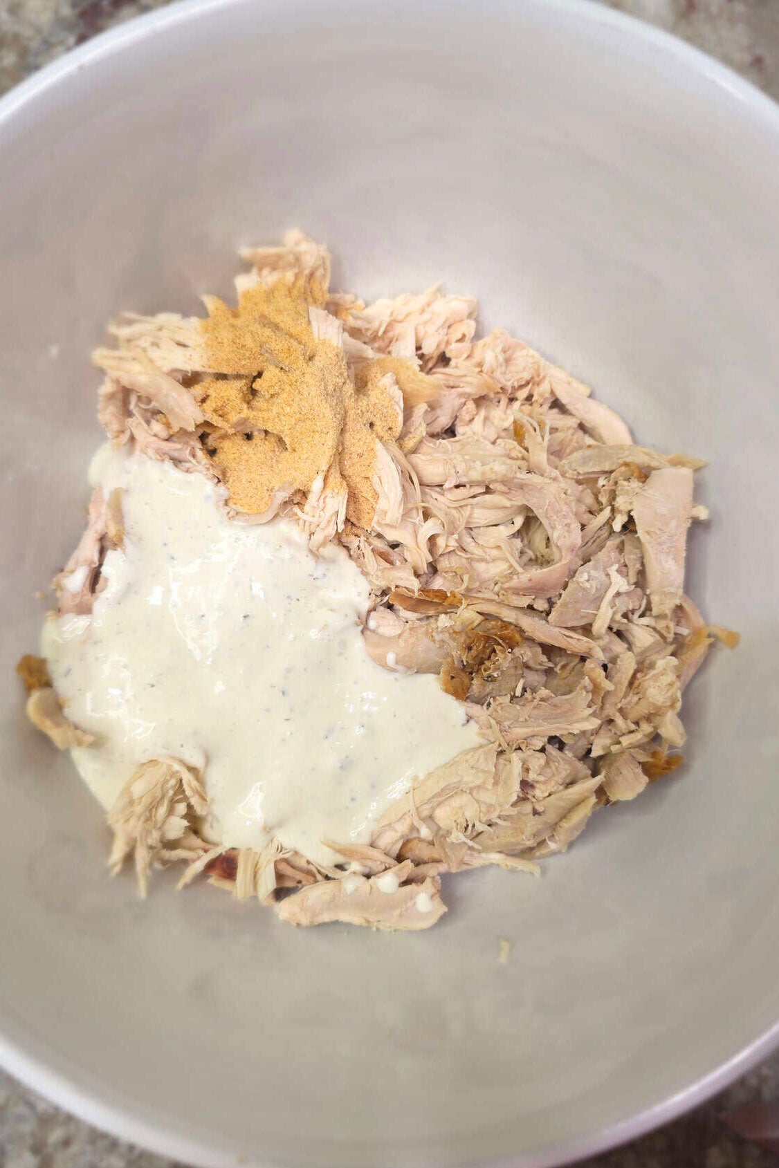 shredded rotisserie chicken in a white bowl with ranch dressing and spices