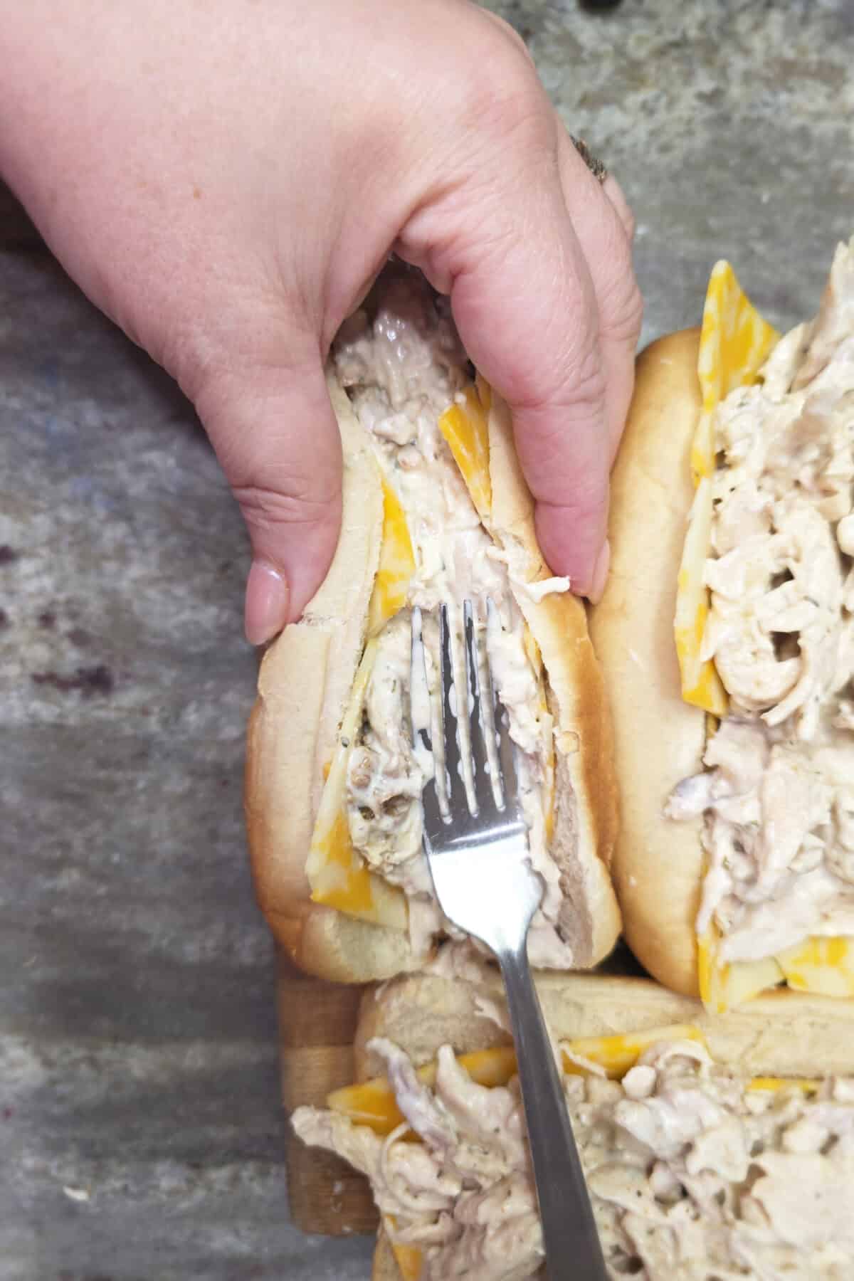 using a fork to press the chicken into the sub roll to close it up tightly