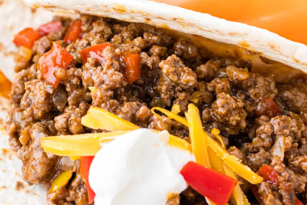 taco meat in a tortilla with yellow and red peppers