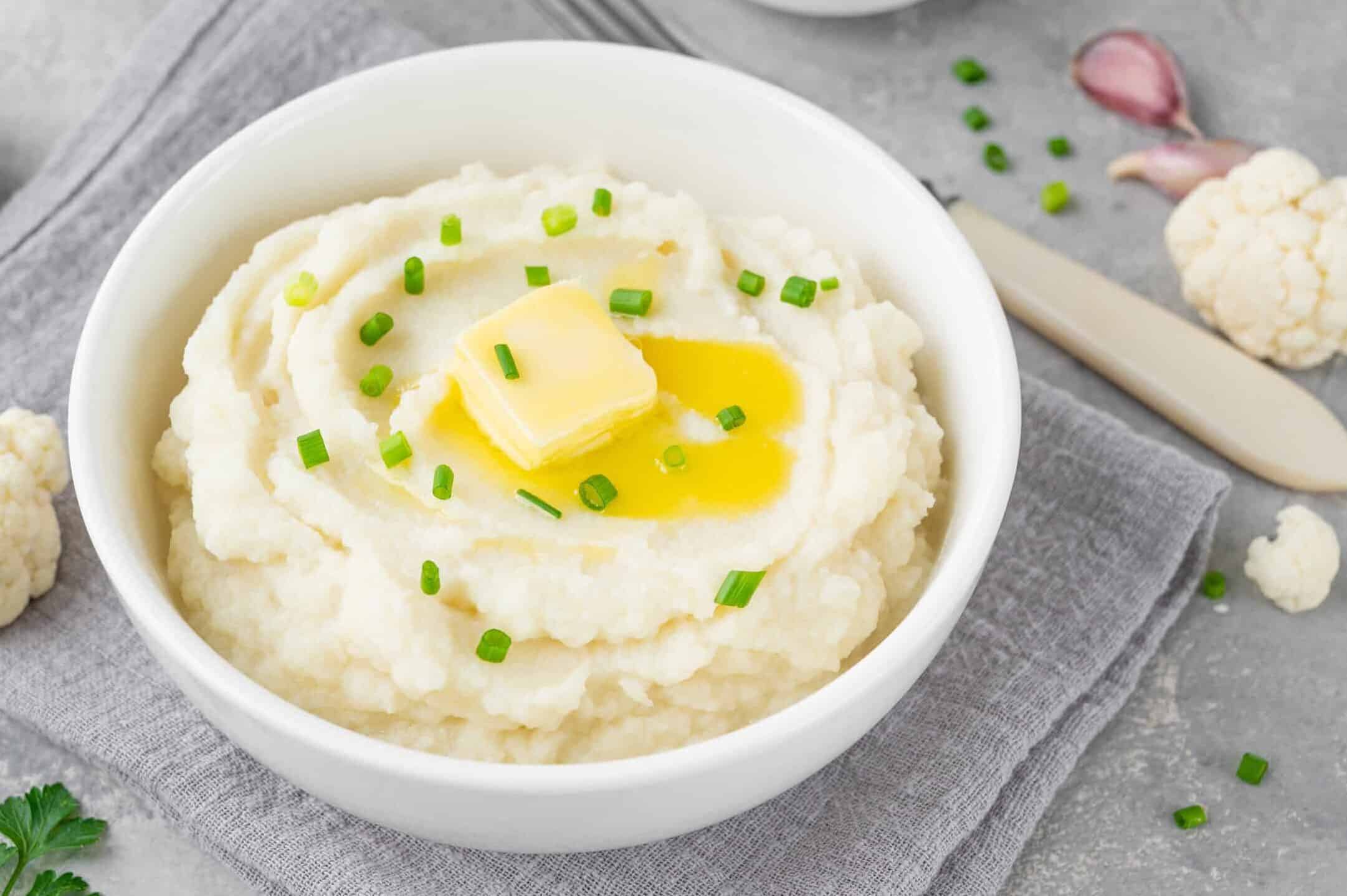 mashed cauliflower in a white bowl with butter and chives
