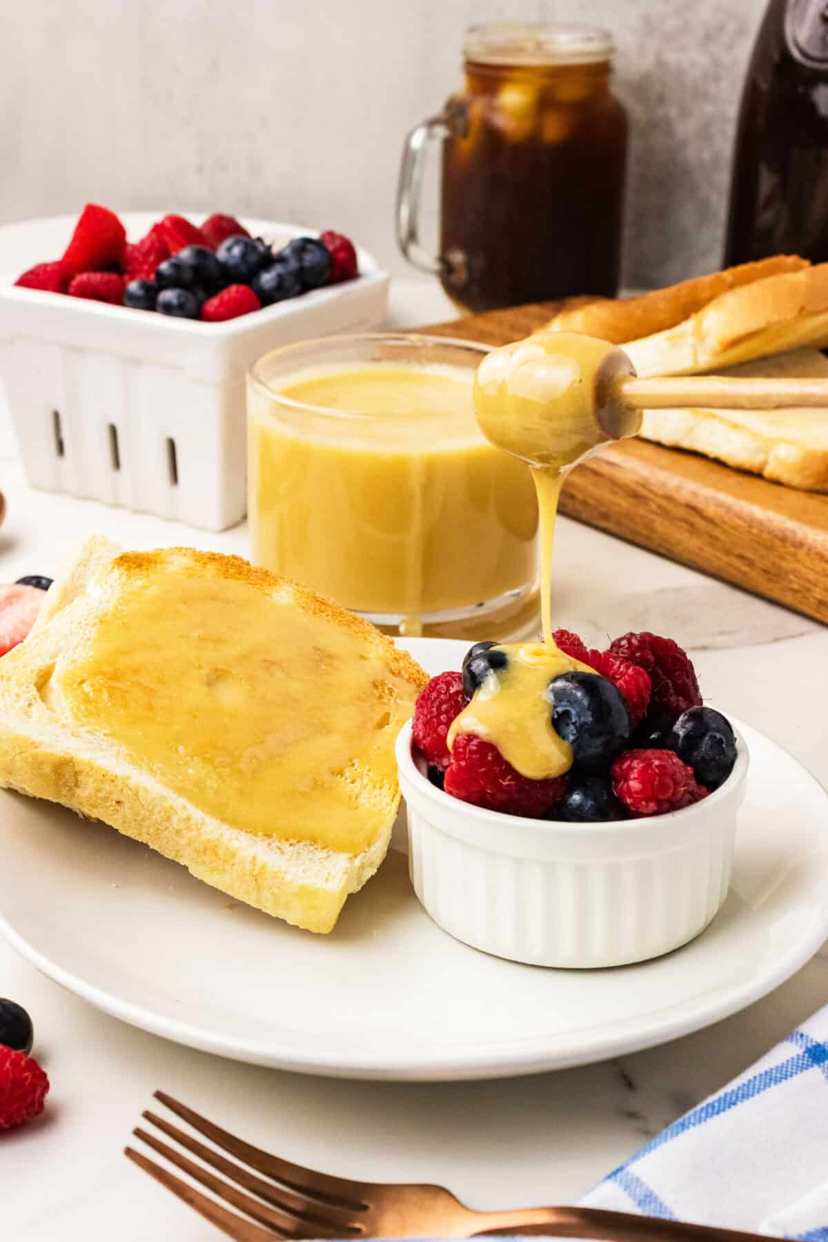 a bowl of fruit with honey being drizzled over it next to honey toast