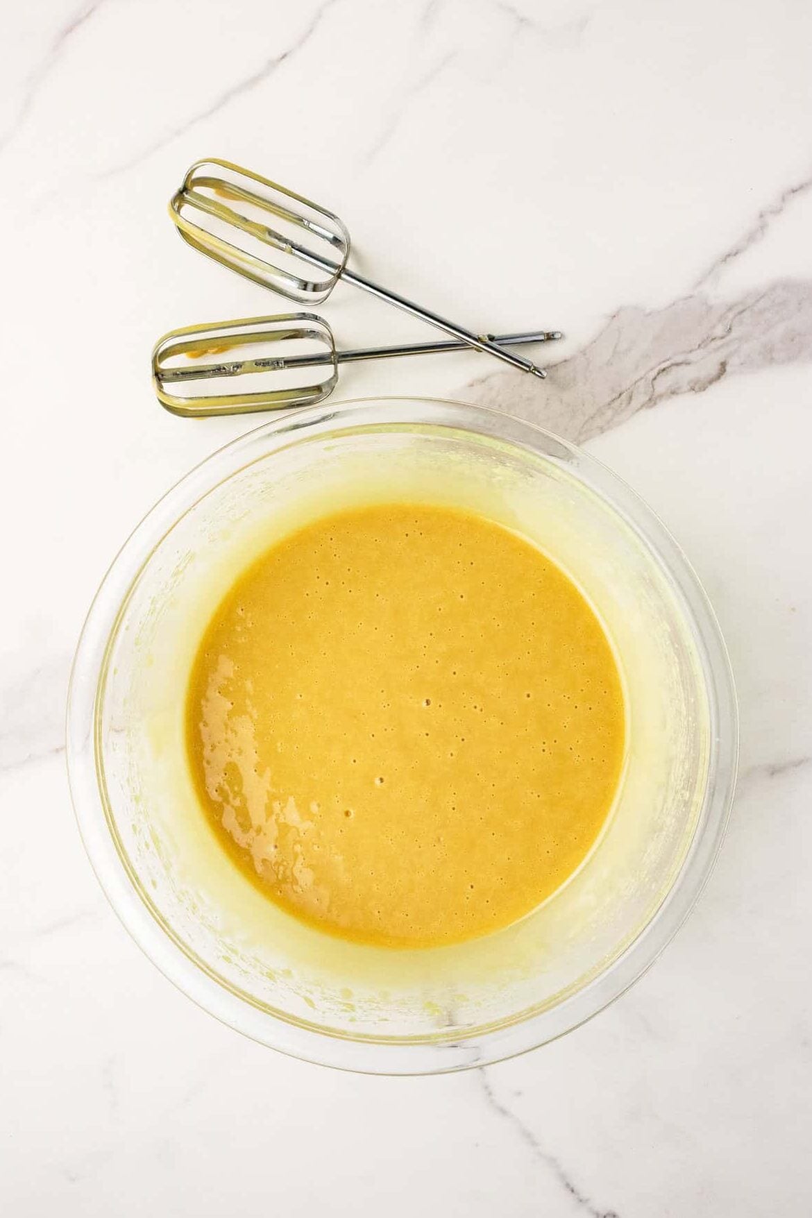 raw honey whipped in a mixing bowl with beater blades next to it on the counter