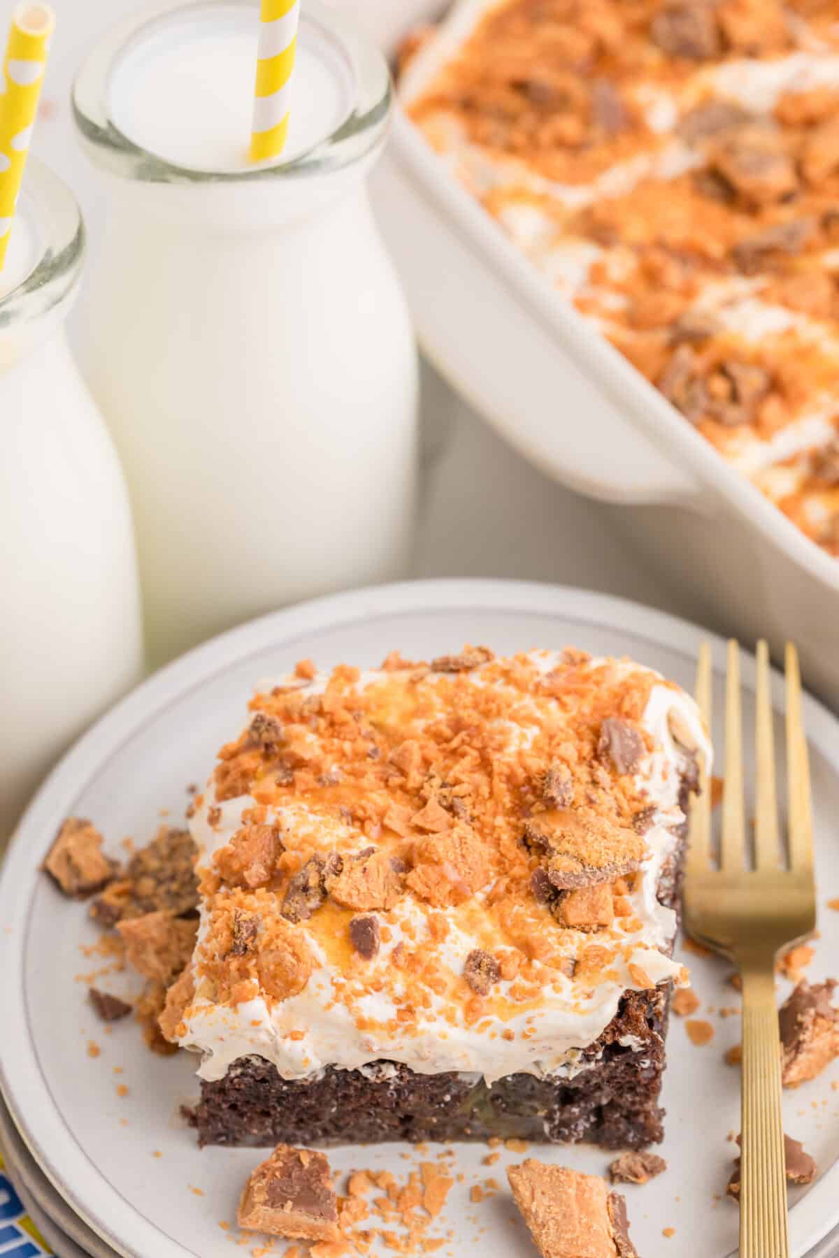 a slice of butterfinger poke cake on a plate next to bottles of milk