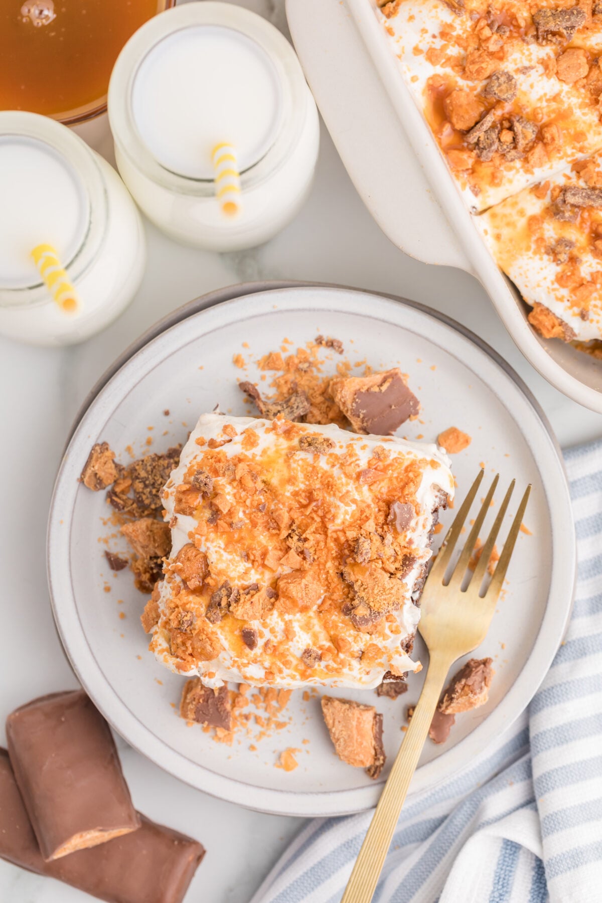 a slice of butterfinger poke cake on a plate next to bottles of milk