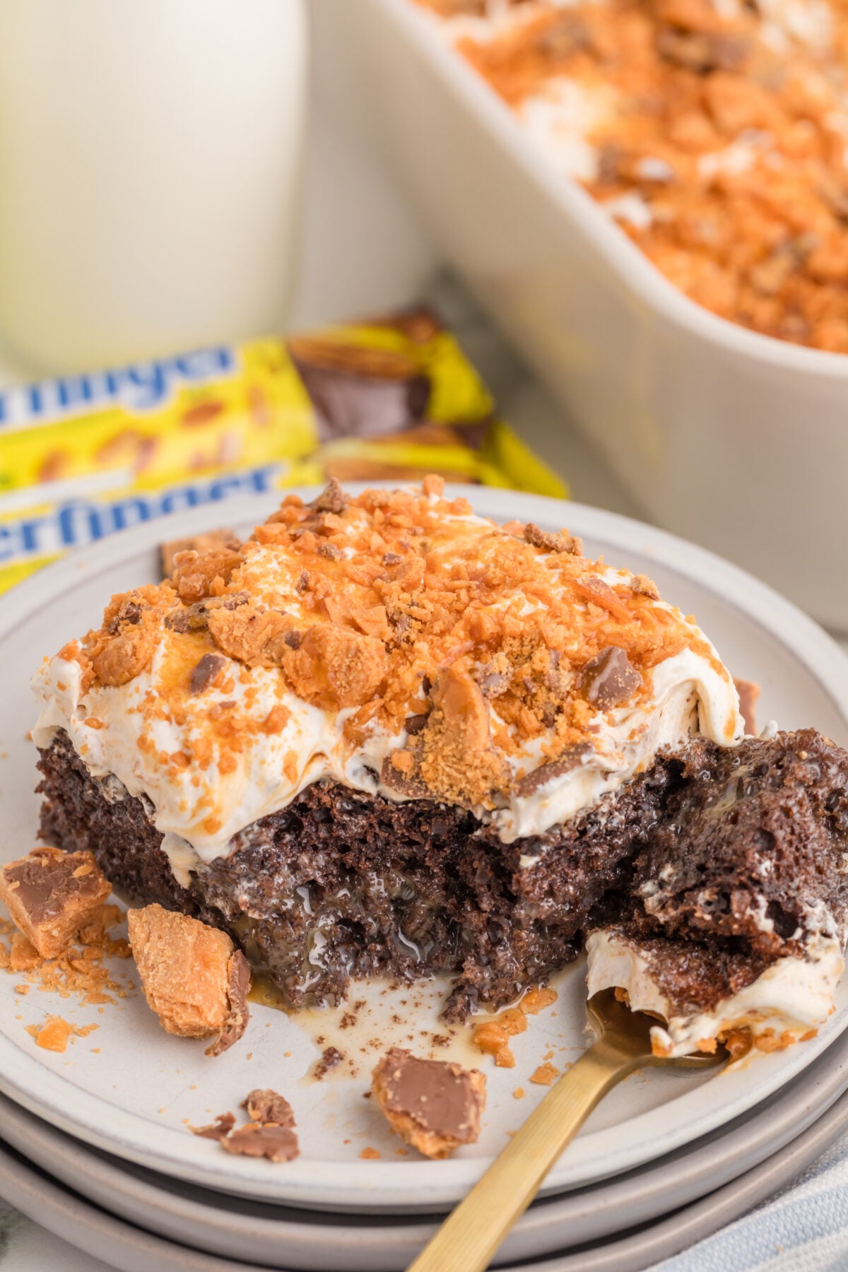 a slice of butterfinger poke cake on a plate next to bottles of milk