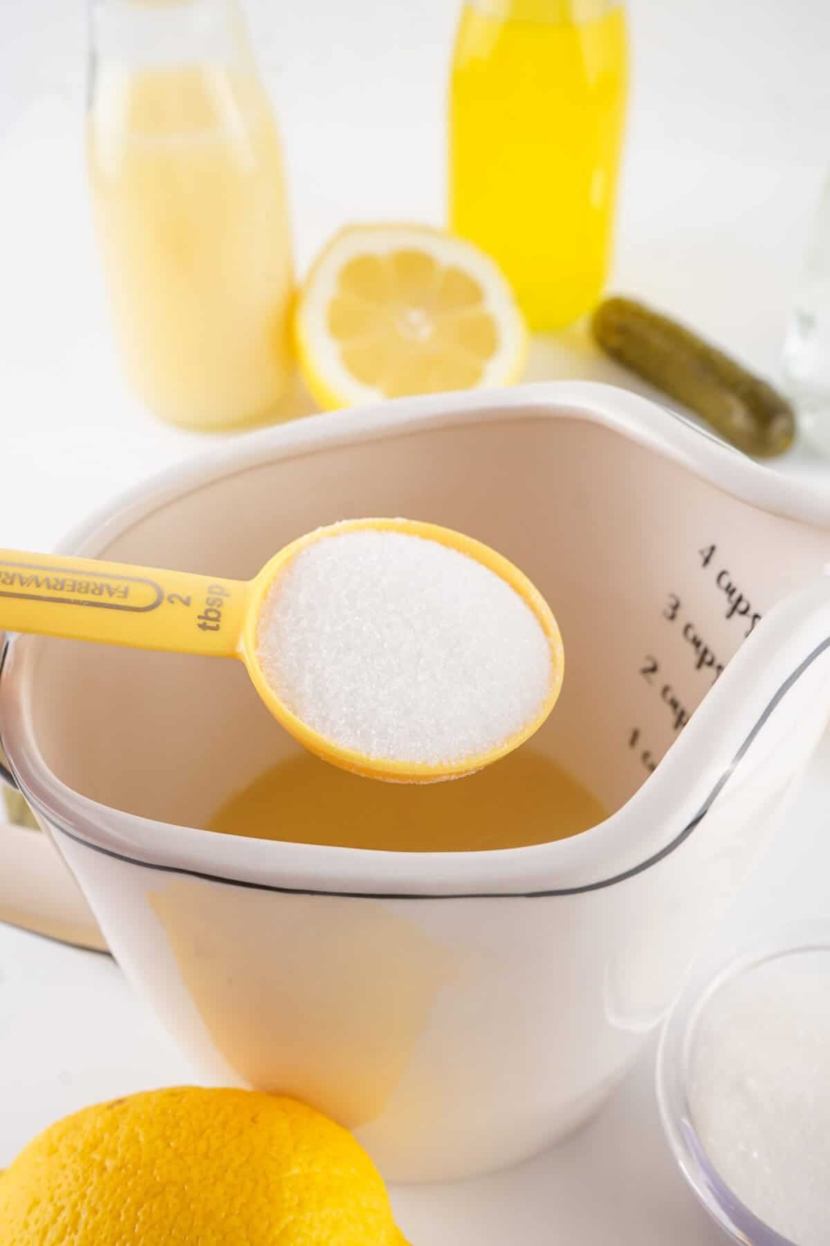 sugar being added to lemon juice in measuring cup