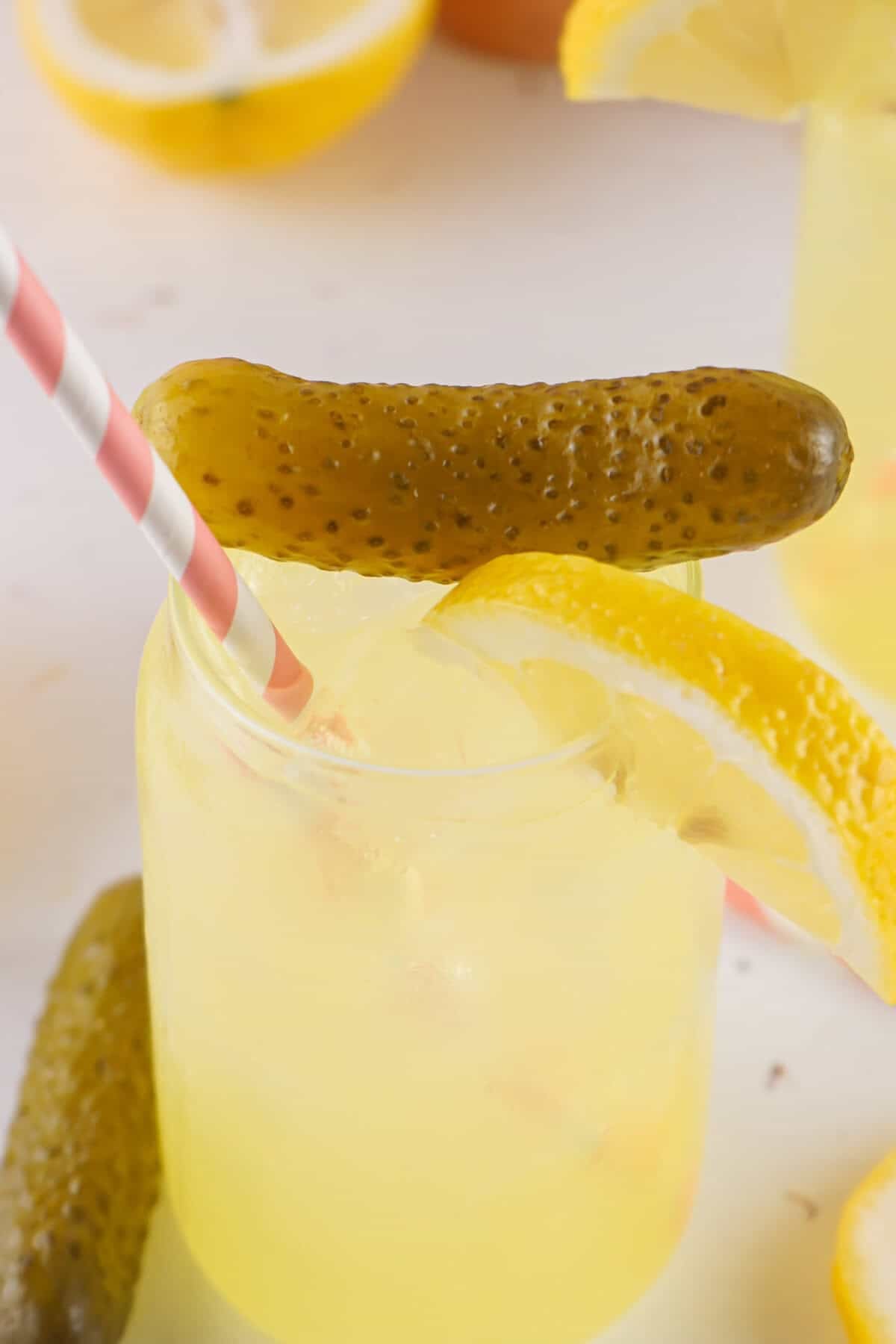 dill pickle lemonade in a glass with pickles and lemons and a pink straw