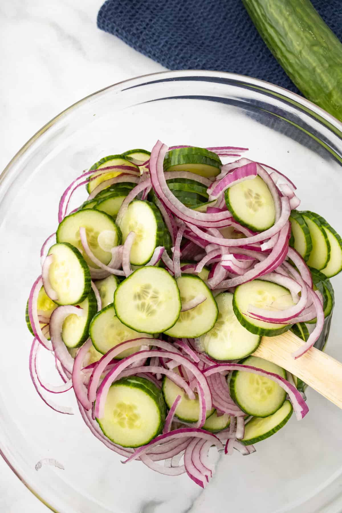 onions and cucumbers in a bowl mixed up and with dressing and a spoon