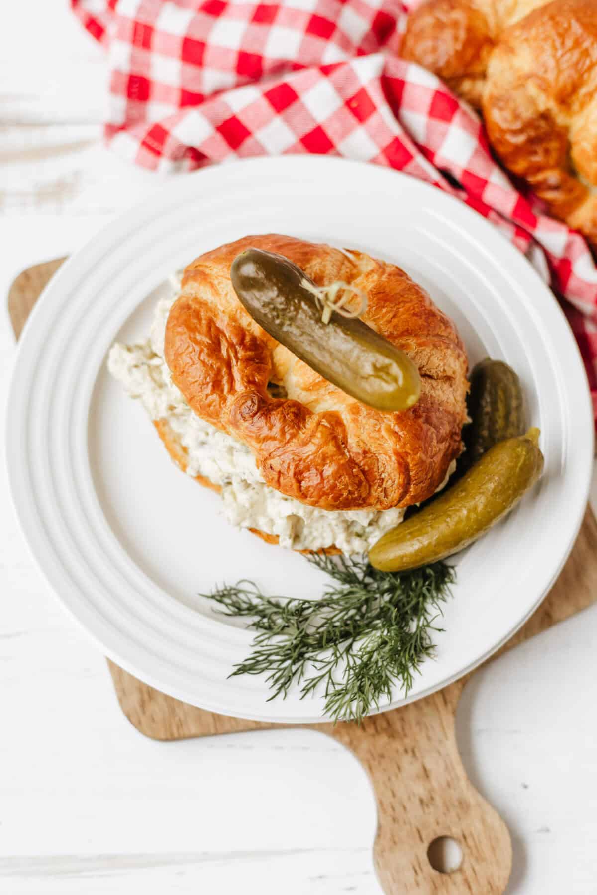 dill pickle chicken salad on a croissant with a pickle on top