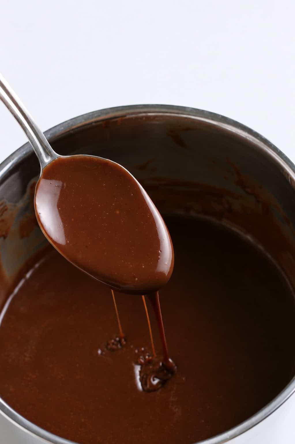 hot fudge sauce dripping off a spoon over a saucepan