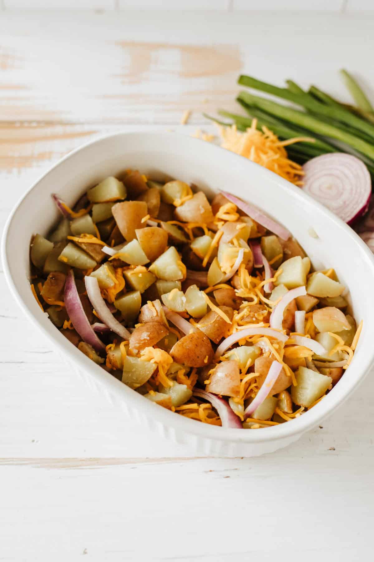 In a separate large bowl, combine the diced potatoes, chopped onion, and shredded cheddar cheese in serving dish with bacon
