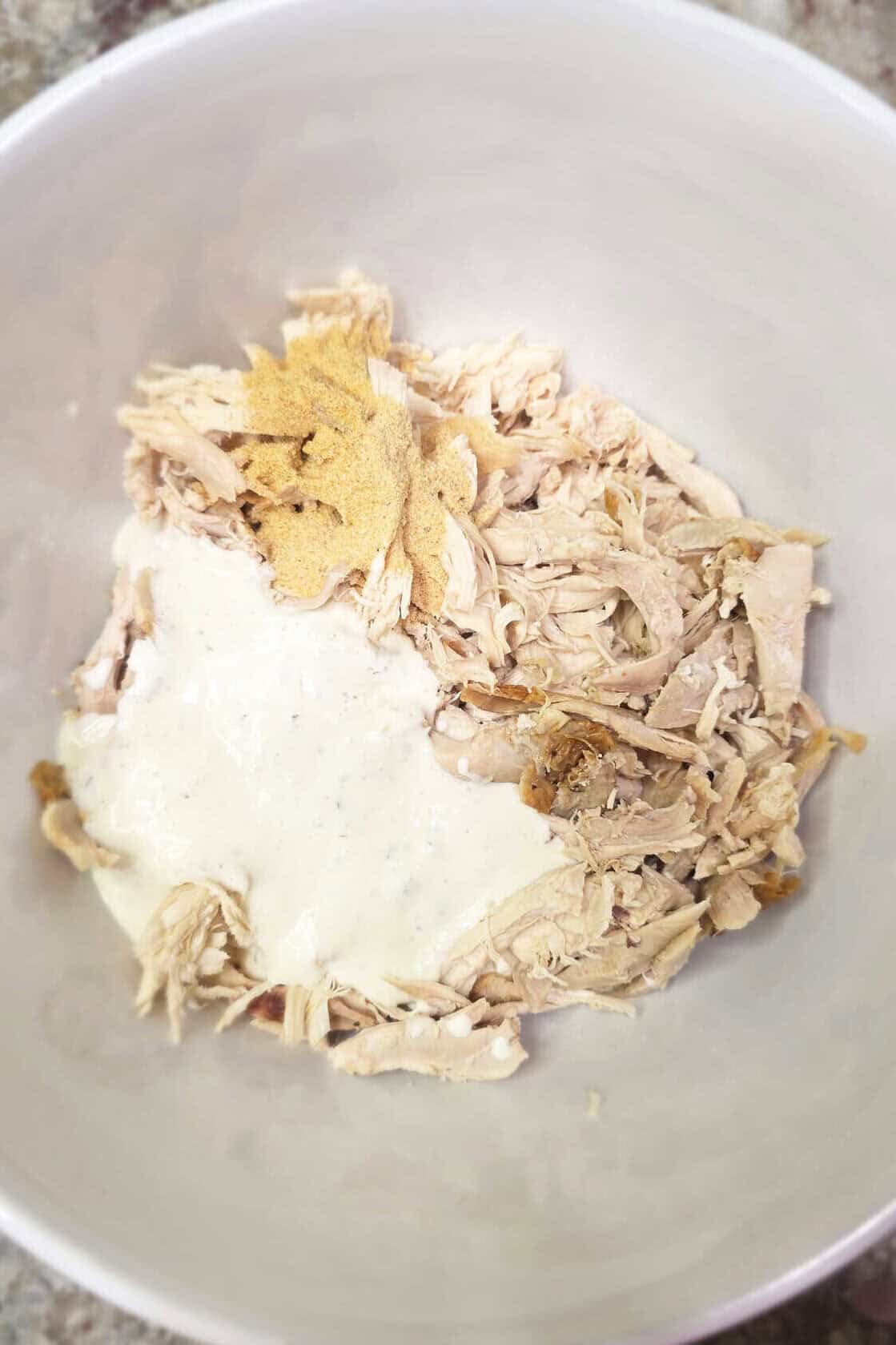 shredded rotisserie chicken in a white bowl coated with ranch and spices
