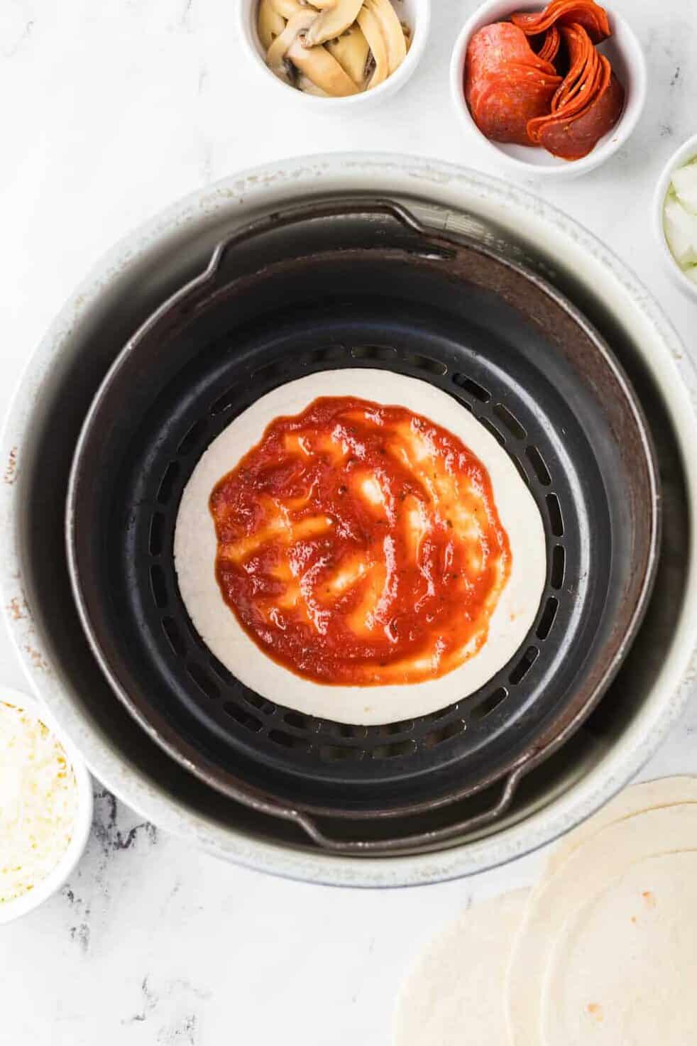 tortilla in air fryer basket with pizza sauce