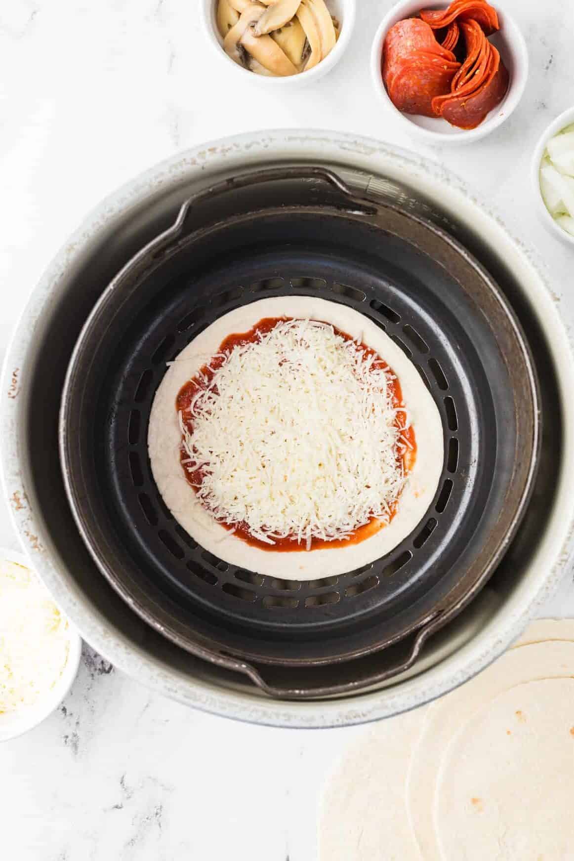 tortilla in air fryer basket with pizza sauce and mozzarella cheese