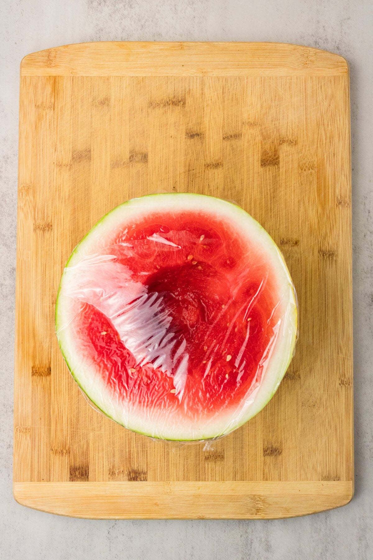 plastic wrap covering half a watermelon with the middle scooped out