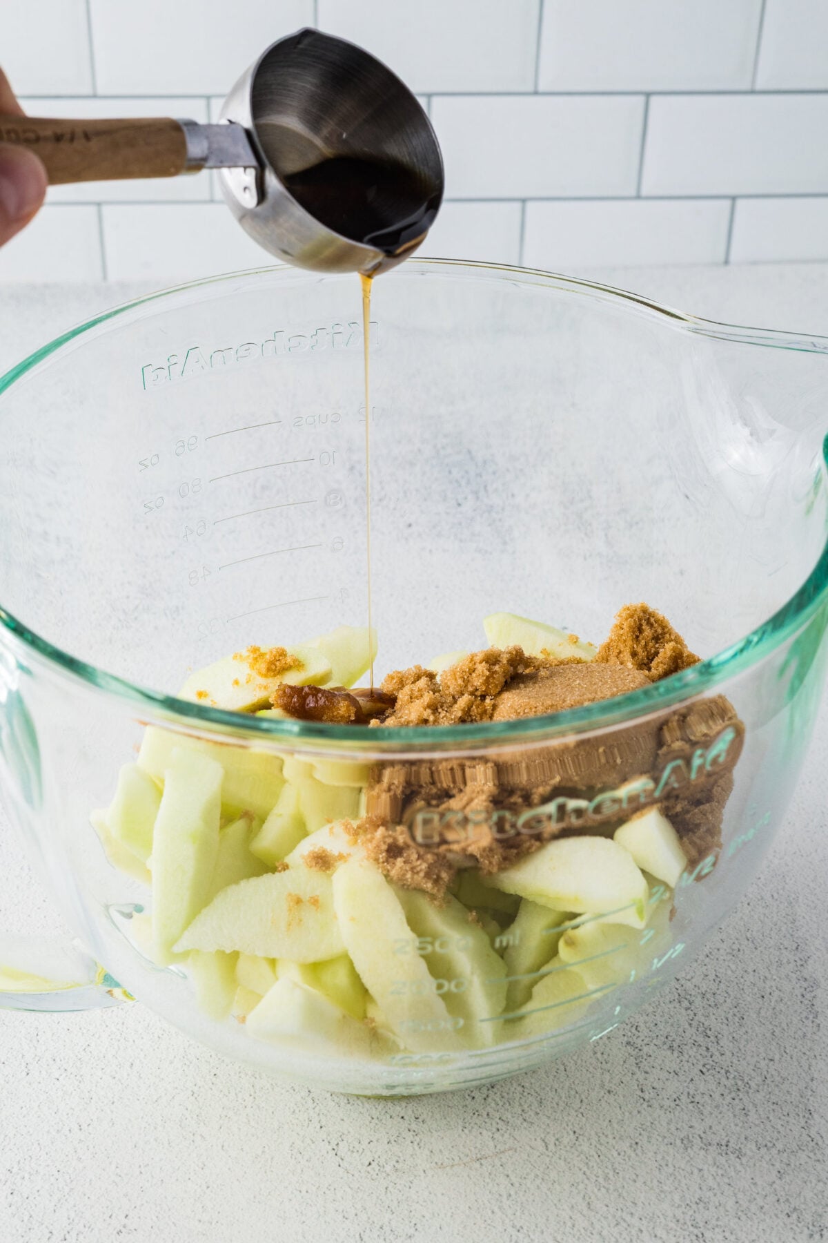 adding brown sugar, maple syrup, and cinnamon to sliced apples in a bowl