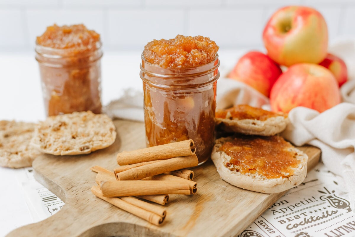 apple jam in a small jar surrounded by cinnamon sticks, apples and biscuits