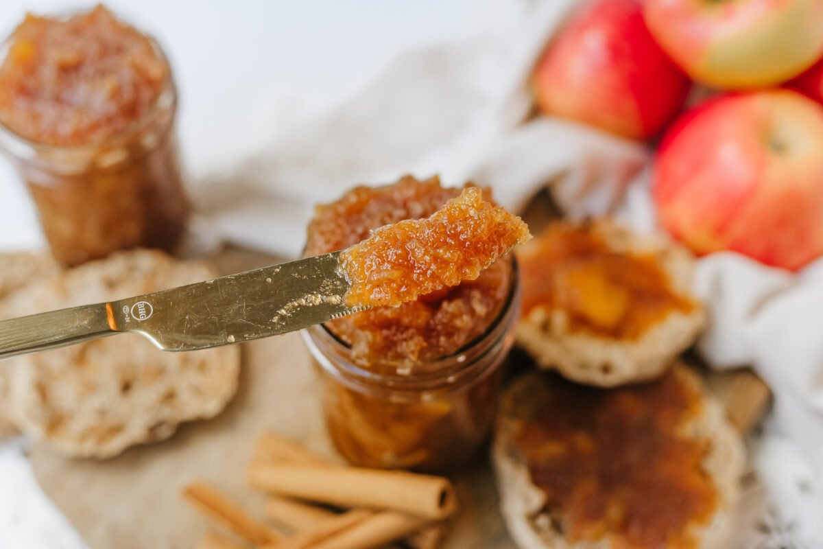 apple jam in a jar with a butter knife of it on top