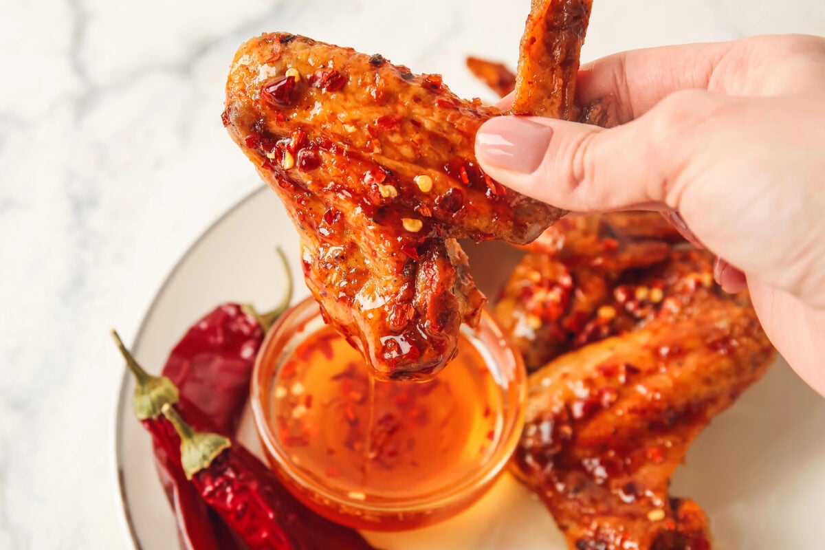 fried chicken wing being dipped in hot honey