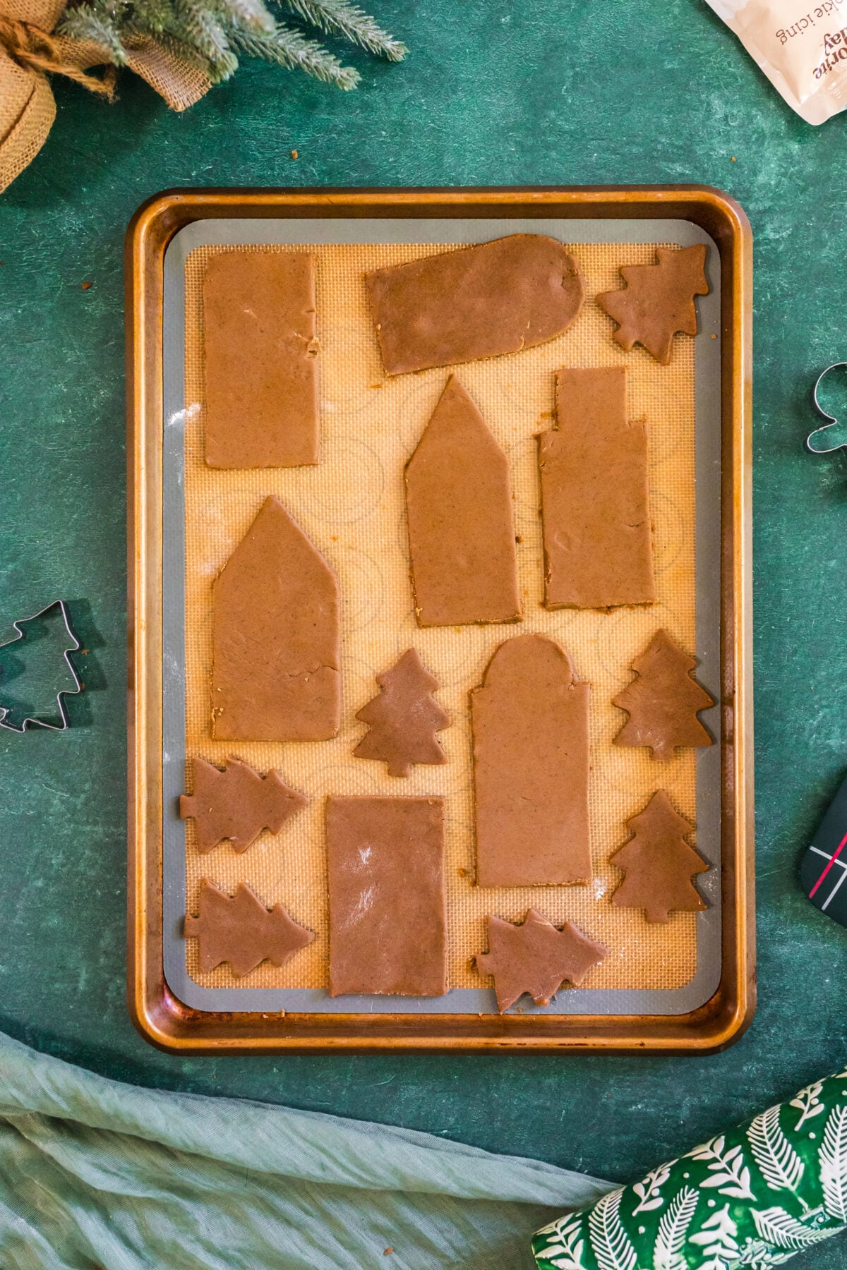 gingerbread houses and trees cut out on parchment on baking sheet