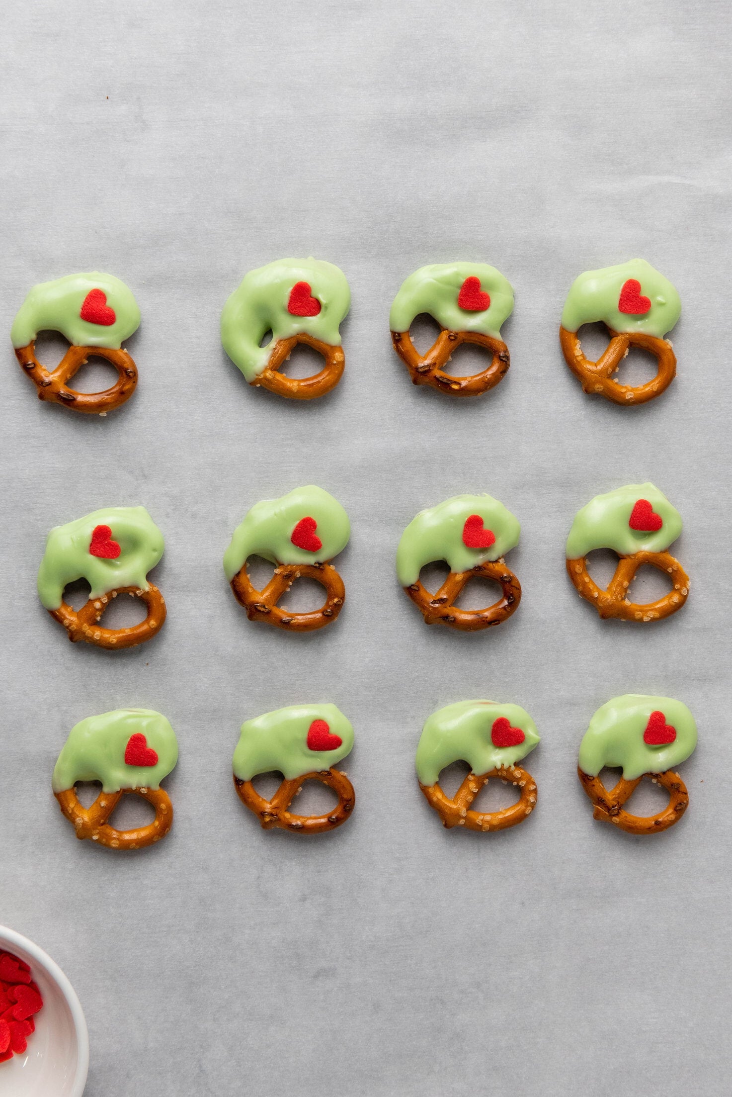 pretzels dipped in green candy melts with a red heart on parchment paper