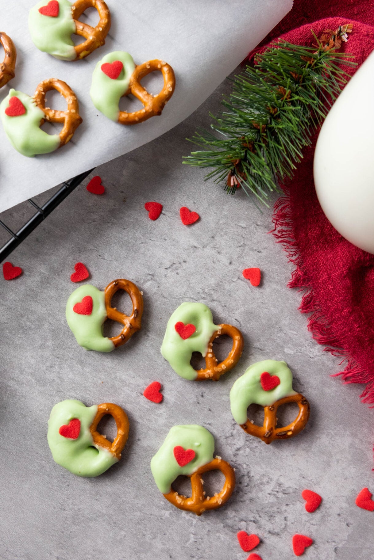grinch pretzels on parchment and a counter top with red heart sprinkles