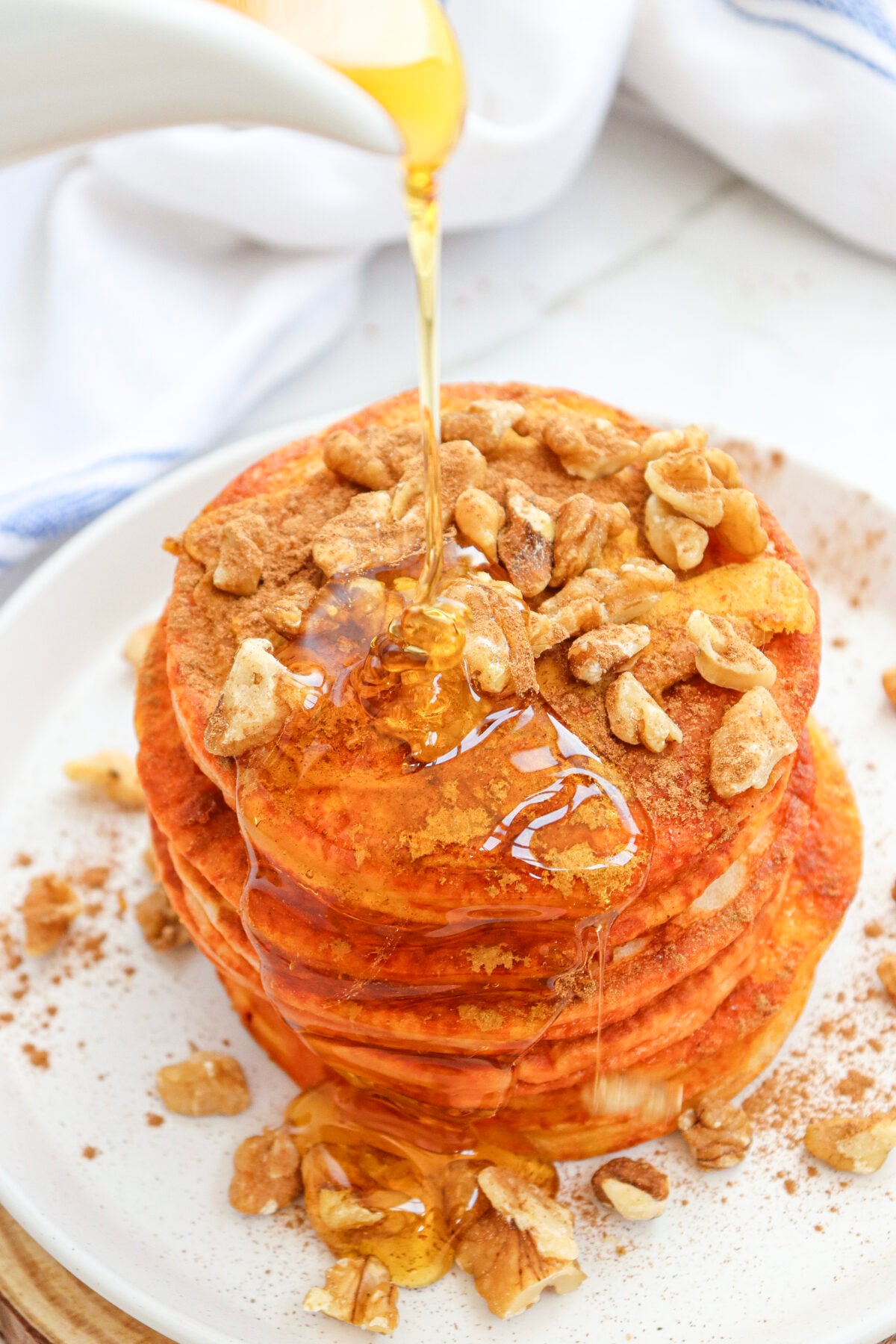 syrup being poured onto pumpkin pancakes with cinnamon and walnuts